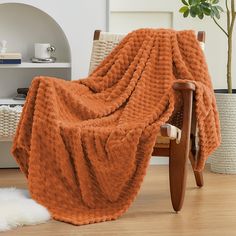 an orange blanket sitting on top of a wooden chair next to a white sheepskin rug