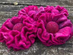 two pink flowers sitting on top of a wooden table next to a piece of wood