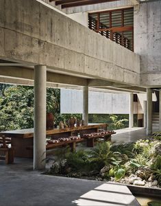 an outdoor dining area with tables and benches under a large concrete structure in the background