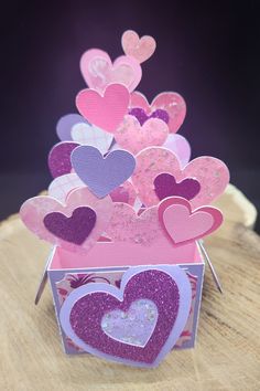 there is a box that has hearts in it on top of a wooden table with purple and pink colors