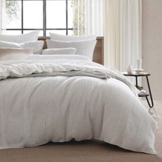 a bed with white linens and pillows in a room next to a large window