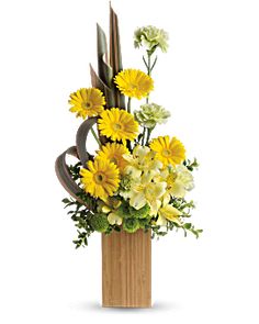 a vase filled with yellow and white flowers on top of a wooden block in front of a