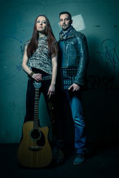 two people standing next to each other with a guitar in front of them and graffiti on the wall behind them