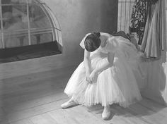 an old photo of a woman in a tutu skirt sitting on the floor looking down