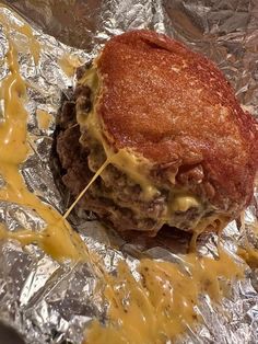 a hamburger covered in cheese sitting on top of aluminum foil with mustard drizzled around it