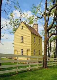 a yellow house sitting on top of a lush green field next to a white fence