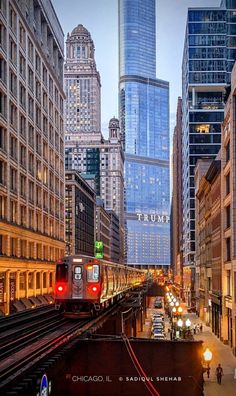 a train traveling through a large city next to tall buildings with skyscrapers in the background