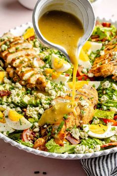 someone pouring dressing onto a salad in a bowl