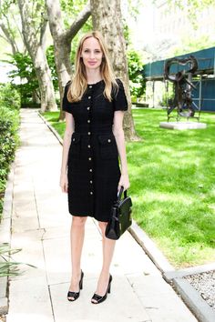 a woman is standing on the sidewalk in a black dress and heels with her hands in her pockets