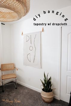 a white room with a chair and hanging tapestry on the wall next to a potted plant