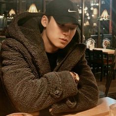 a young man sitting at a table with his arms crossed and wearing a black hat