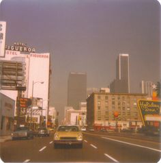 a yellow car driving down a city street next to tall buildings and neon signs in the distance