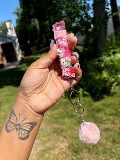 a hand holding a pink keychain with hello kitty on it and a pom - pom