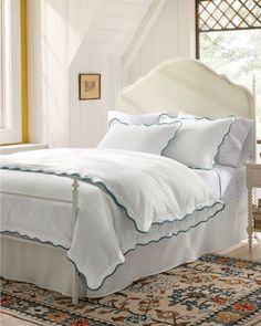 a bed with white sheets and blue trim on the headboard is in a bedroom