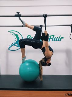 a woman is doing aerial exercises on a gym ball while hanging upside down from the ceiling