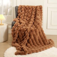 a fluffy brown blanket is sitting on a chair next to a table with a lamp