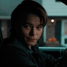 a young man sitting in the driver's seat of a car with his hand on the steering wheel