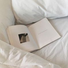 an open book sitting on top of a bed next to white sheets and pillow covers