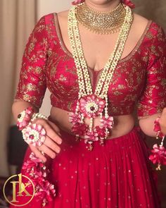 a woman in a red dress with flowers on her chest and necklaces around her neck