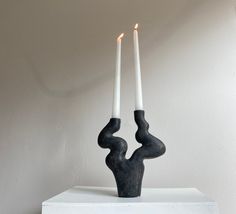 two white candles sitting on top of a table next to a black sculpture with one candle in the shape of a human hand