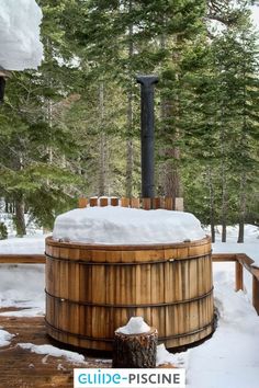 a wooden hot tub sitting on top of a snow covered ground next to pine trees