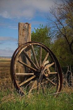 an old wooden wagon wheel leaning against a fence post in the middle of a field