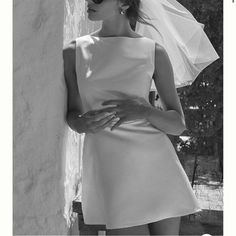 a woman in a short white dress and veil leaning against a wall with her hands on her hips