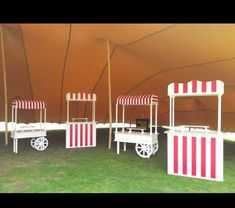 three white and red striped carts sitting on top of a grass covered field next to a tent