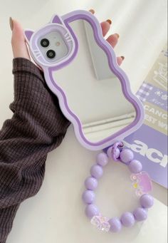 a woman's hand holding a cell phone case next to a purple beaded bracelet