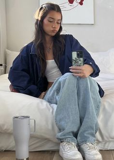 a woman sitting on top of a bed holding a cell phone next to a cup