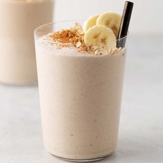 two glasses filled with smoothie and topped with banana slices, granola and cinnamon