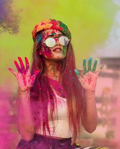 a woman is covered in colored powder and holding her hands up to the side with both hands