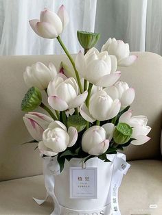 a bouquet of white tulips in a vase on a table next to a couch