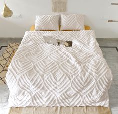 a bed with white bedspread and pillows on top of it in a room