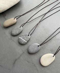 Handmade beach stone necklace , the sea pebble have been hand drilled and threaded onto a extra strong silk string, the end of string have a gray colour gemstone each side.  Pendant size:  Style 1: 1.2cm x 3.5cm Style 2: 1.8cm x 3.0cm Style 3: 2.1cm x 3cm Style 4: 1.9cm x 2.8cm Style 5: 2cm x 3.2cm A 2.4 x 3.5cm B 2 x 3.2cm C 2.2 x 3.6cm D 2.5 x 3.4cm E 1.8 x 3.5cm F 1.8 x 3.8cm G 1.6 x 4cm H 2 x 3cm I 2 x 3cm J 1.8 x 3.6cm the necklace is adjustable can be worn long and short, one size to fits all. The shape and colour of stone are completely natural, each piece is one of a kind. A Great natural gift for all ages. Beach Stones Jewelry, Pebble Jewelry, Pebble Pendant, J 1, Pebble Necklace, Stone Ornaments, Stone Art Painting, Rock Necklace, Stone Jewellery