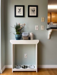 a white table with two pictures on the wall and a dog bowl underneath it in front of a mirror