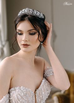 a woman wearing a tiara and holding her hair in one hand while looking at the camera