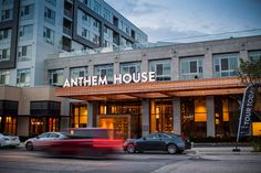 cars drive past an apartment building with the name's sign on it at dusk