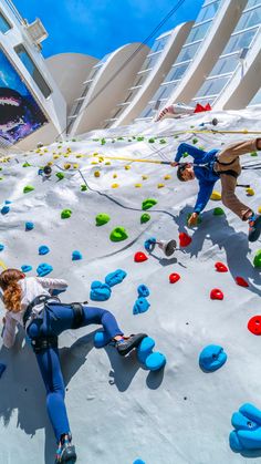 two people are climbing up and down the rock wall at an indoor climbing area in front of a building