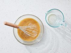 a whisk in a glass bowl next to a measuring cup filled with liquid