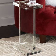 a clear glass table with a red chair in the background and a white rug on the floor