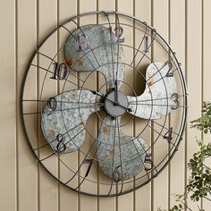 a metal clock mounted to the side of a wall next to a potted plant