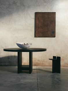 a black table with a white bowl on it in front of a brown wall and a painting