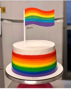 a rainbow colored cake with a flag on top is sitting on a table in front of a refrigerator