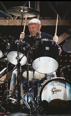 an older man playing drums on stage with other drummer's equipment in the background