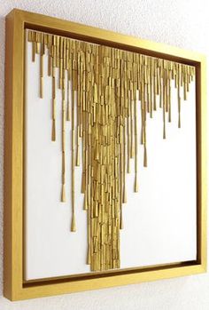 a gold framed art piece hanging on the side of a white wall with wooden sticks sticking out of it