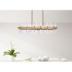 a modern chandelier hangs over a dining room table with white dishes and vases