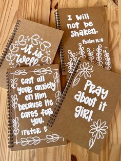 three brown notebooks with white writing on them sitting on a wooden table next to each other