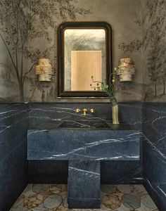 a bathroom with a marble counter top and wall papered walls, along with a large mirror above the sink