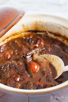 a pot full of stew with a wooden spoon in it and the lid partially open